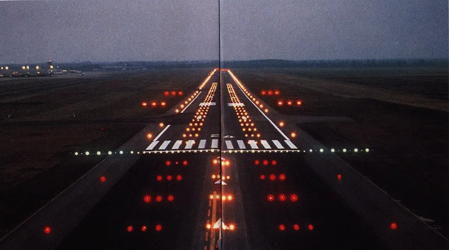 A runway lit up at dusk, seen head-on, its approach lights converging toward the horizon.
